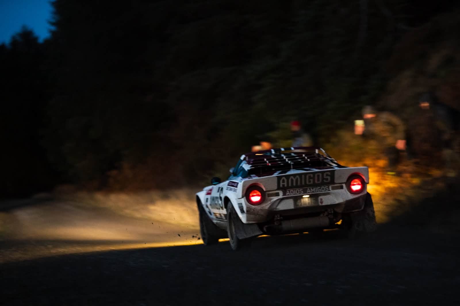 The Amigos-liveried Perez Lancia Stratos on a gravel forest stage at dusk